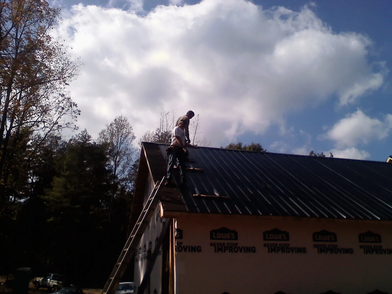 Roofer fastening dark metal panels high against a cloudy sky, from a Roof Inspection job in Farmington